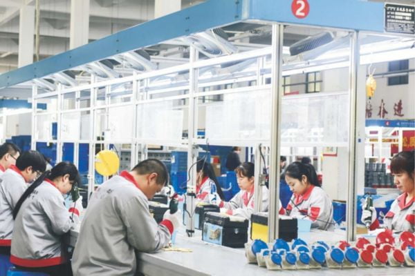 A factory worker assembling an industrial plug on a production line